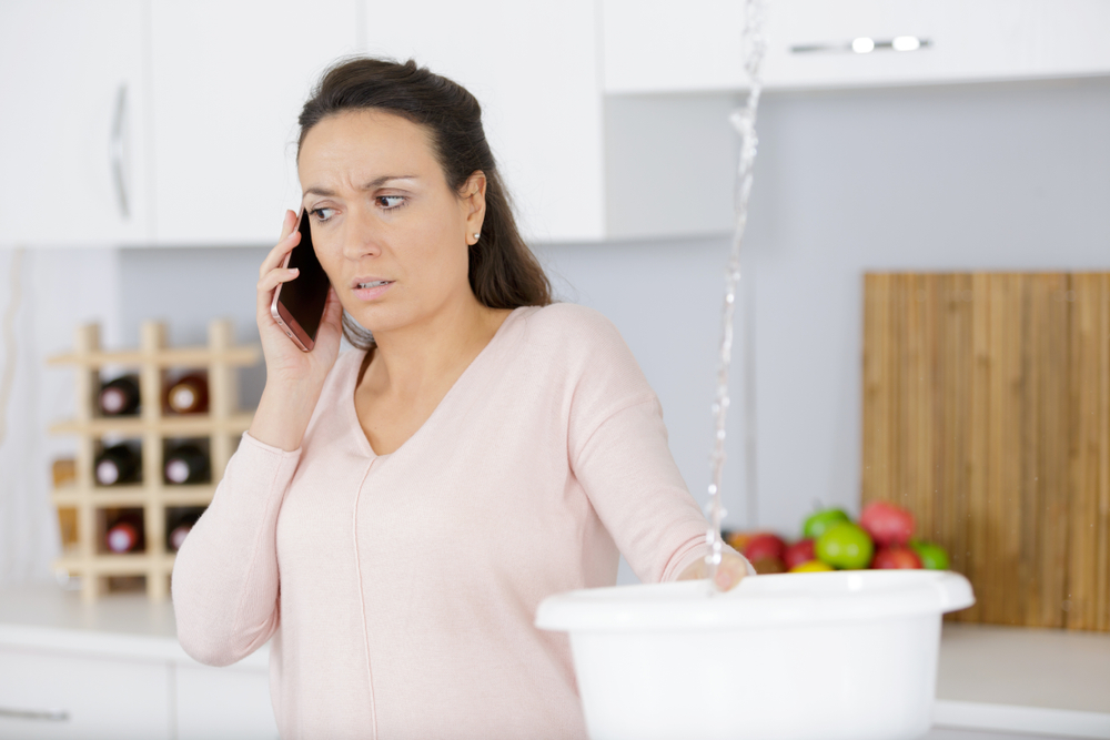 woman on the phone while holding bucket for water leak