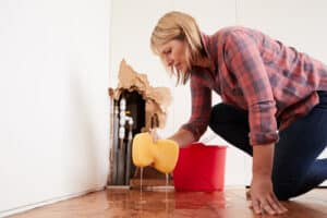 woman cleaning up water leak from bursted water pipe